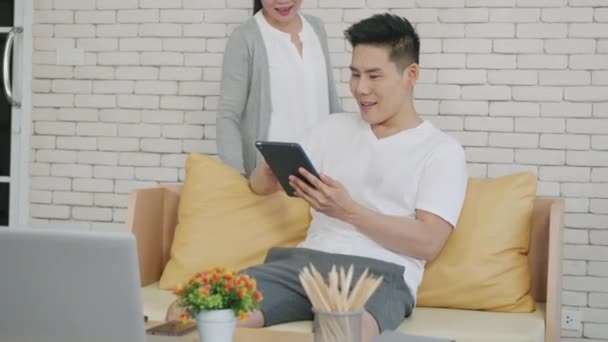 幸せなアジアの家族のカップルの夫と妻の仕事と議論のためのデジタルタブレットを使用しています 明るく愛情のあるカップルは オンラインで何かを買い物し リビングルームで自宅から一緒にソーシャルメディアを見て笑顔 — ストック動画