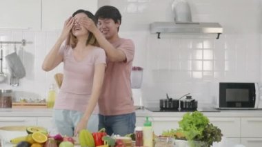 Mutlu Asyalı güzel aile çifti karı koca mutfakta salata pişiriyorlar. Adamın yaptığı sürpriz salata yemeği için gözlerini kapatan kadın. sağlıklı gıda konsepti