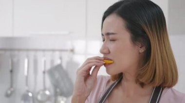 Asyalı genç ve mutlu bir kadının portresi mutfaktaki taze limon mutfağını ısırıyor. Kadın duyguları çok ekşi bir ifade oluşturuyor. Sağlıklı yaşam tarzı kavramı. yavaş çekim