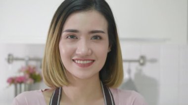 Asyalı genç ve mutlu bir kadının portresi. Mutfakta el ele tutuşurken gülümsüyor. Kameraya bakıyor. Kadın ev hanımı kollarını kavuşturup lüks içinde yemek yapıyor. yavaş çekim