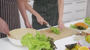 Mutlu Asyalı güzel aile çifti karı koca mutfakta sebze salatası pişiriyorlar. Sebzeleri bir kaba karıştıran adam sebze kesen kadın. sağlıklı gıda konsepti