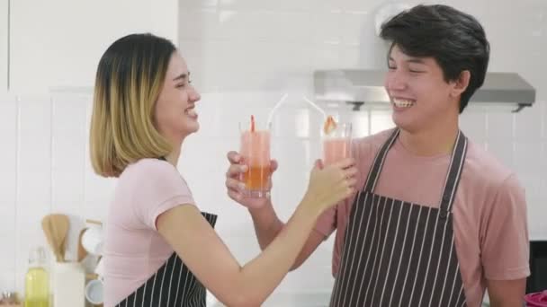 幸せなアジアの美しい若い家族のカップルの夫と妻は家で朝一緒にガラスのキッチンで新鮮なリンゴスムージージュースを飲みながら腕を楽しんでいました 健康的なライフスタイルのコンセプト — ストック動画