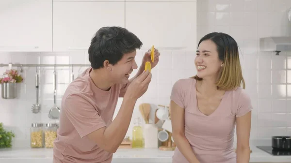快乐的亚洲年轻漂亮的一对夫妻 夫妻欢欢喜喜地微笑着 在男人的眼前 放着一个切好的橙子 在家里的厨房里共度时光 — 图库照片