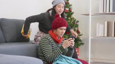 Happy Asian beautiful young family couple husband and wife in home living room, woman hide surprise giving Christmas gift box her boyfriend present, winter holidays and valentine concept. slow motion