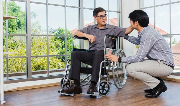 車椅子のアジアの高齢者障害者のビジネスマンは オフィスのチームとの交流について話し合う 車椅子の老人と幼い息子が父と話をして慰めました — ストック写真
