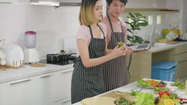 Mutlu Asyalı güzel aile çifti karı koca mutfakta sebze salatası pişiriyorlar. Kadın ve erkek online yemek kursuna göre dizüstü bilgisayardan yemek tarifi
