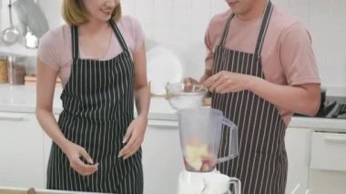 Mutlu Asyalı güzel aile çifti karı koca evde mutfakta taze elma püresi yapıyorlar. Kadın ve erkek meyve suyu karıştırıcısına buz döküyorlar. Sağlıklı yaşam tarzı kavramı