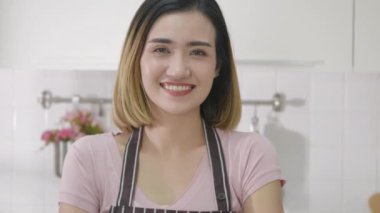 Asyalı genç ve mutlu bir kadının portresi. Mutfakta el ele tutuşurken gülümsüyor. Kameraya bakıyor. Kadın ev hanımı kollarını kavuşturup lüks içinde yemek yapıyor. yavaş çekim