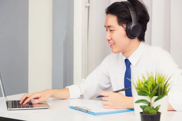 自宅からの仕事 アジアの若いビジネスマンはスーツビデオ会議コールやFacetime彼はノートパソコンを使用して机の上に座って笑って 自宅のオフィスで紙のノートブック情報を書きます — ストック写真