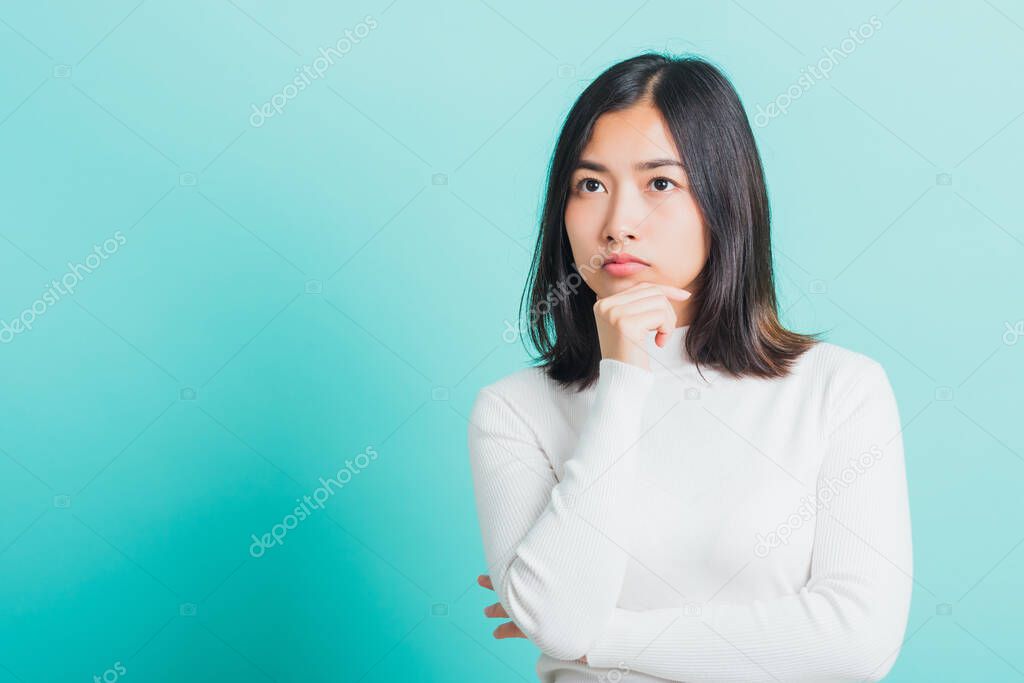 Young beautiful Asian woman hand near the face and thinking, Portrait  female touch chin dream dreamy having doubts, studio shot isolated on a blue background