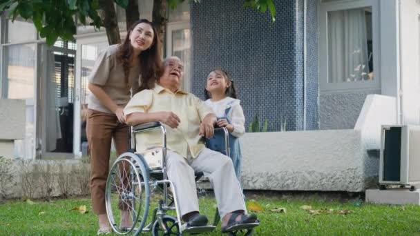 公園で孫と母親と一緒に車椅子で高齢者の障害者のおじいちゃん 幸せなアジアの3世代の家族は屋外の裏庭で一緒に楽しんで おじいちゃんと小さな子供は笑って笑った — ストック動画