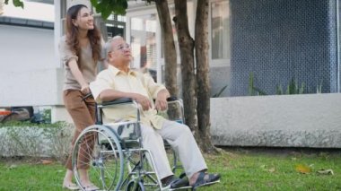 Tekerlekli sandalyede kızıyla oturan sakat, mutlu Asyalı nesil aile arka bahçede eğleniyor yaşlı bir adamı gezdiren, gülen ve ağır çekimde yardım eden genç bir kadın.