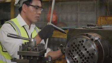 Asyalı profesyonel mekanik operatör üniforma takıyor ve koruyucu gözlük takıyor. Güvenlik görevlileri atölye metal torna fabrikası, sanayi, ağır çekim, ağır çekim...