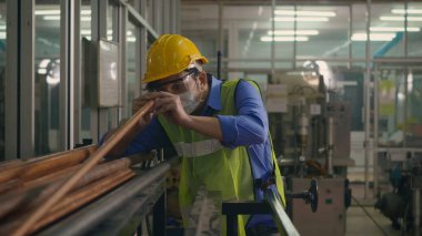 Korumalı kask üniforması giyen Asyalı fabrika işçisi veya mühendis üretim endüstrisinin deposundaki çelik boru malzemelerine bakın.