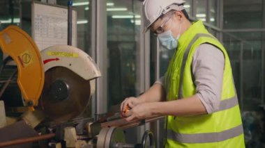 Fabrika sanayi işçileri teknisyeni veya mühendis üniforma giyer, güvenlik kaskları çelik boruyu ölçmek için atölyedeki bir kesici aletle kesmeden önce bir mezura kullanır.