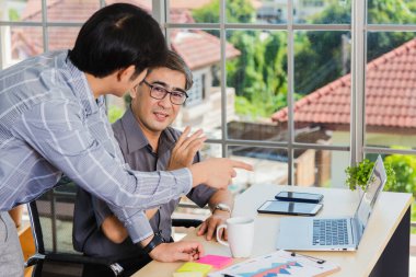 Modern bir dizüstü bilgisayarda çalışan Asyalı kıdemli ve genç iş adamı ekran toplantısına internetten bakıyor. Eski ve kıdemsiz işadamı ofisindeki masada video konferansını kullanıyor.