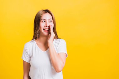 Asya Taylandlı mutlu bir portre güzel bir kadın tişört giyer dudaklarına el ele tutuşur gizli dedikodular fısıldar izole edilmiş fotoğraf stüdyosuna bakar sarı arka planda fotokopi çekilir