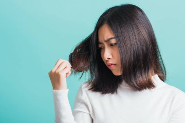 Genç ve güzel Asyalı bir kadın tarağı ve sorunlu saçı yüzünden üzgün, portre kadın saç dökülmesi sorunu yaşıyor, stüdyo çekimi mavi arka planda, sağlık konseptinde izole edilmiş.