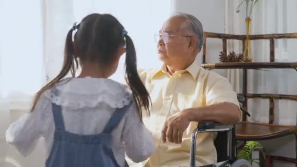Asiatische ältere Person sitzt einsam im Rollstuhl, kranke Enkelin läuft herbei und hält einen Papiervogel, mit dem sie spielen und ermutigen kann, Glückliche alte Frau mit kleinem Kind