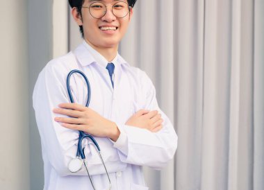 Mutlu Asyalı yakışıklı doktorun portresi. Üniformalı yakışıklı adam. Kolları çapraz duruyor. Steteskop elinde.