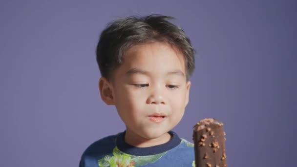 肖像画幸せなアジアの笑顔の小さな子供の男の子チョコレートアイスクリームを食べて 子供の食べ物を楽しむ甘いアイスクリーム孤立紫色の背景を食べる — ストック動画