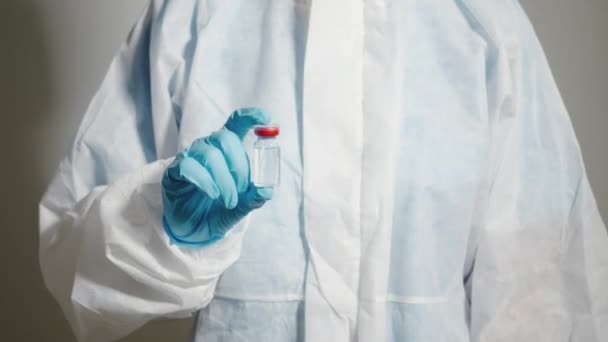 Ppeスイートの女性医師または科学者の密接な手ラボで青い手袋保護を身に着けている制服手に薬液体ワクチン瓶 コロナウイルスまたはCovid 19医療コンセプト — ストック動画
