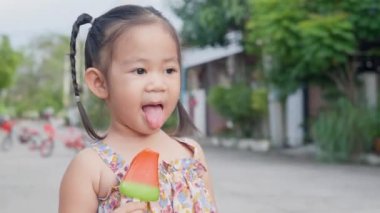 Küçük tatlı çocukların portresi dondurma yemekten, açık havada gülümsemekten ve yaz boyunca kırmızı buzlu dondurma yiyen Asyalı çocuğun portresi. Komik Bebek Yiyen Dondurma