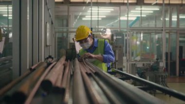Korumalı kask üniforması giyen Asyalı fabrika işçisi veya mühendis üretim endüstrisinin deposundaki çelik boru malzemelerine bakın.