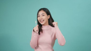 Asyalı genç ve güzel bir kadın gülümsüyor diş fırçalarken müzik dinliyor, dişlerini fırçalıyor şarkı söylüyor, dans ediyor ve eğleniyor mavi arka planda izole edilmiş, yaşam tarzı diş hijyeni ve sağlık konsepti.