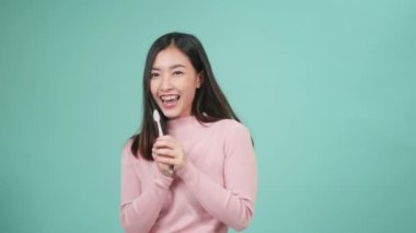 Asyalı genç ve güzel bir kadın gülümsüyor diş fırçalama dansı yapıyor müzikten hoşlanıyor, dişleri fırçalayan dişler şarkı söylüyor, dans ediyor ve eğleniyor mavi arka planda izole edilmiş, yaşam tarzı diş sağlığı, yavaş çekim