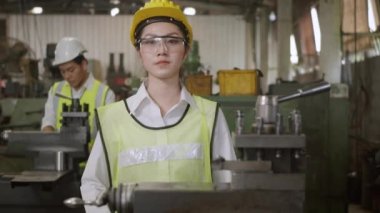 Asyalı mühendis kadın işçinin portresi güvenlik gözlüğü takıyor. Makineyi kontrol ediyor. Endüstriyel üretim fabrikası çapraz kollu gülümsüyor.