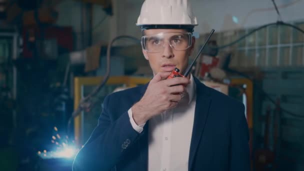 专业有信心的工程师商人穿着西服 手握对讲机站在重工业厂房制造中 用钢制焊接机器人 火花放电 慢动作 — 图库视频影像