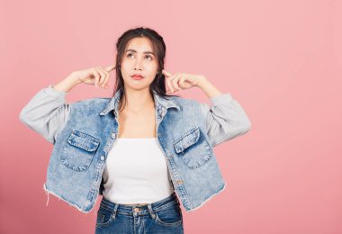 Asya portresi güzel hoş bir genç kadın, kulak tıkayıcı kulaklar takıyor, dinlemek istemiyor, stüdyo çekimi pembe arka planda, Taylandlı kadın kulakları fotokopi alanı ile kaplıyor.