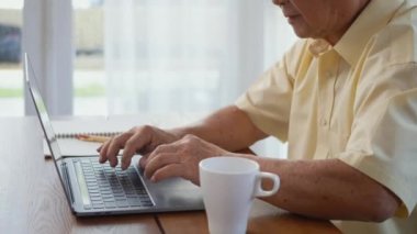 Üst düzey adam gözlük takıyor, sandalyede oturuyor evdeki dizüstü bilgisayarda çalışıyor, mutlu yaşlı adam emekli oluyor, yaşlı büyükbaba evde çalışıyor.