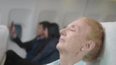 Yolcu erişkin iş kadını uykulu, yaşlı, uçakta battaniyeli, seyahat sırasında yaşlı bir kadın uçak koltuğunda uyuyor.