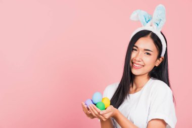 Mutlu Paskalyalar. Elinde renkli Paskalya yumurtaları tutan tavşan kulağı takan güzel bir genç kadın, kameraya bakan bir portre kadın, pembe arka planda izole edilmiş bir stüdyo resmi.