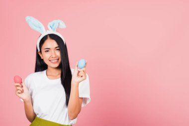 Mutlu Paskalyalar. Elinde renkli Paskalya yumurtaları tutan tavşan kulağı takan güzel bir genç kadın, kameraya bakan bir portre kadın, pembe arka planda izole edilmiş bir stüdyo resmi.