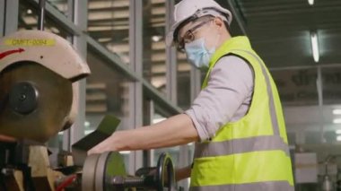 Fabrika sanayi işçileri teknisyeni veya mühendis üniforma giyer, güvenlik kaskları çelik boruyu ölçmek için atölyedeki bir kesici aletle kesmeden önce bir mezura kullanır.