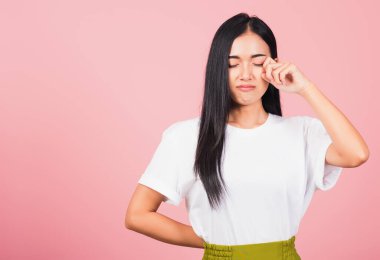 Asya portresi güzel tatlı genç kadın kötü ruh hali gözyaşlarını parmaklarıyla siliyor, stüdyo çekimleri pembe arka planda izole edilmiş, Taylandlı kadın üzgün hissediyor fotokopi uzayı ile ağlayan mutsuz.