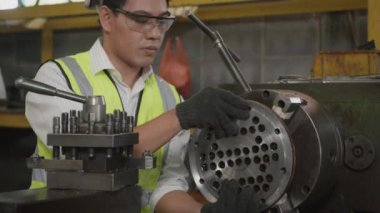 Asyalı profesyonel mekanik operatör üniforma takıyor ve koruyucu gözlük takıyor. Güvenlik görevlileri atölye metal torna fabrikası, sanayi, ağır çekim, ağır çekim...