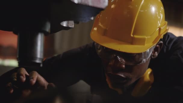 フロントマシンでの検査のための黄色のヘルメットと耳保護監視を持つアメリカの産業用黒の若い労働者の男 工業工場でのエンジニア検査チェック作業 スローモーション — ストック動画
