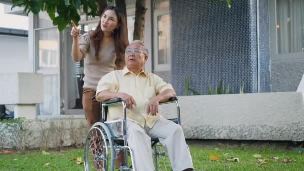 公園の娘と車椅子で障害のあるシニア男性 屋外の裏庭で一緒に楽しんでいる幸せなアジアの世代の家族 ケアヘルパー若い女性が笑顔で高齢者の男性を歩くと笑った — ストック動画