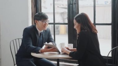 Mutlu iki genç işadamı ve kadın başarılı bir toplantı sonrasında el sıkışıyor ya da dijital tabletle masaya oturuyor, iş adamları tartışıyor ve öğle yemeğinde gülümsüyor.