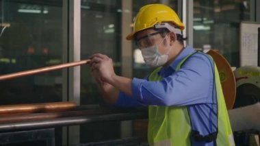 Korumalı kask üniforması giyen Asyalı fabrika işçisi veya mühendis üretim endüstrisinin deposundaki çelik boru malzemelerine bakın.