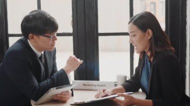 Mutlu iki Asyalı genç işadamı ve kadın buluşmadan önce el sıkışıyor veya dijital tabletle masaya oturuyor, iş adamlarının planlarını tartışıyor ve gülümsüyor.