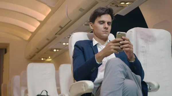 Businessman sitting inside plane watching video on mobile phone during his business trip, Young passenger man using smartphone on airplane while traveling for safe flight
