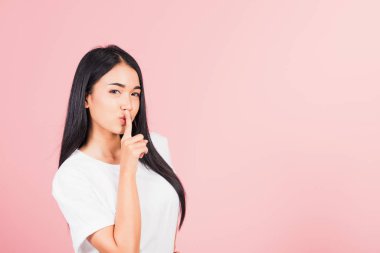 Asyalı mutlu bir portre güzel tatlı bir genç kadın gülümsüyor parmaklarını dudaklarına koyuyor sessiz bir jest stüdyosu çekimleri pembe arka planda izole edilmiş Taylandlı kadın fotokopi çekimleri için kameraya bakıyor.