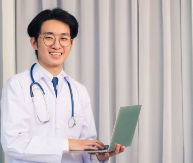 Doktor elbisesi giyen ve steteskop gülümseyen Asyalı genç doktor portresi, sağlık hizmetleri konsepti.