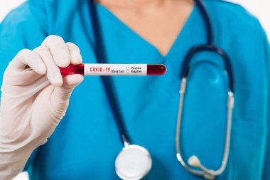 Mavi üniformalı hemşire laboratuarda beyaz arka planda izole edilmiş Coronavirus test kanını, COVID-19 ilaç salgın konseptini incelemek için bir maske takıyor.