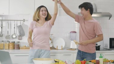 Mutlu Asyalı güzel aile çifti karı koca mutfaktaki mutfak gereçleri mikrofonlarında şarkı söyleyip evde dans ederek eğleniyorlar. Dans eden iki kişi